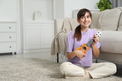 Photo of Happy woman playing ukulele on floor at home, space for text