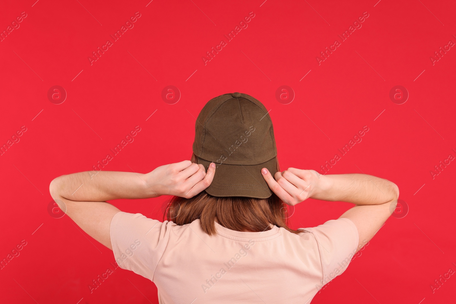 Photo of Woman in stylish baseball cap on red background, back view. Mockup for design