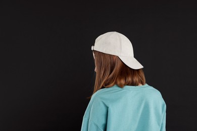 Photo of Woman in stylish baseball cap on black background, back view. Mockup for design