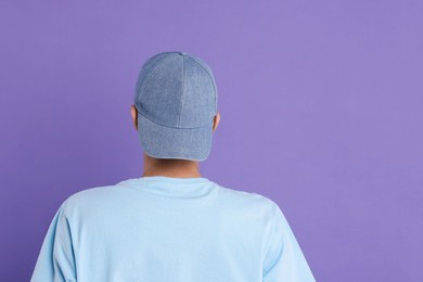 Photo of Man in stylish baseball cap on violet background, back view. Mockup for design