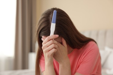 Photo of Upset woman with negative pregnancy test at home, space for text