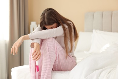 Photo of Upset woman with negative pregnancy test on bed at home