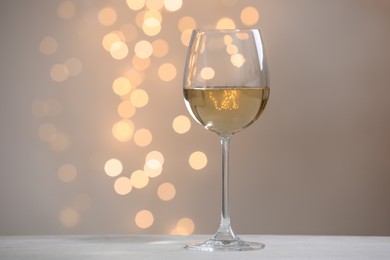 Photo of Tasty white wine in glass on table against grey background with blurred lights, bokeh effect. Space for text