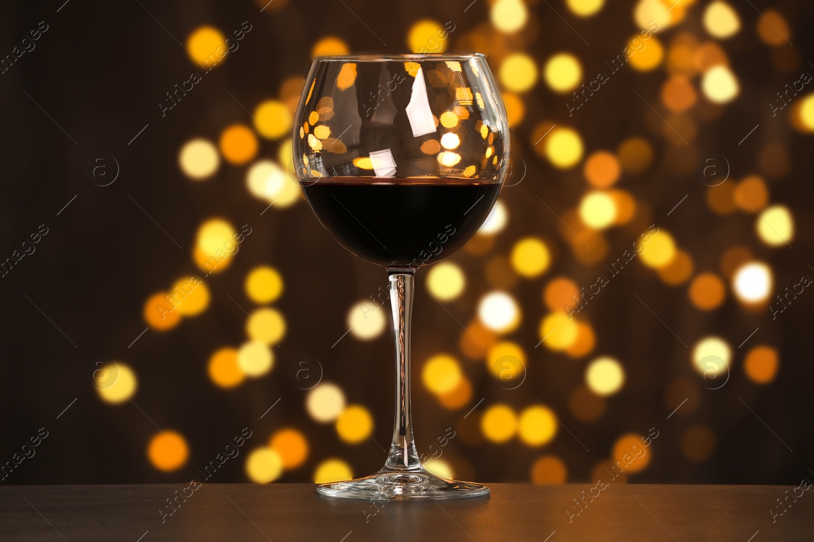 Photo of Tasty red wine in glass on table against dark background with blurred lights, bokeh effect