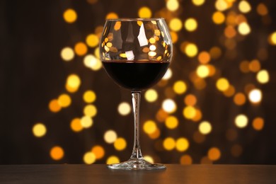 Photo of Tasty red wine in glass on table against dark background with blurred lights, bokeh effect