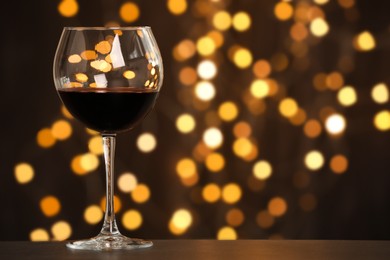 Photo of Tasty red wine in glass on table against dark background with blurred lights, bokeh effect. Space for text