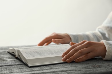 Photo of Woman with open Holy Bible in English language at wooden table, closeup