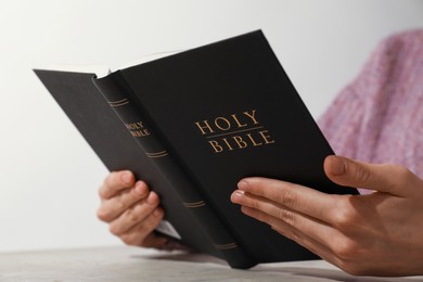 Photo of Woman reading Holy Bible at beige table, closeup