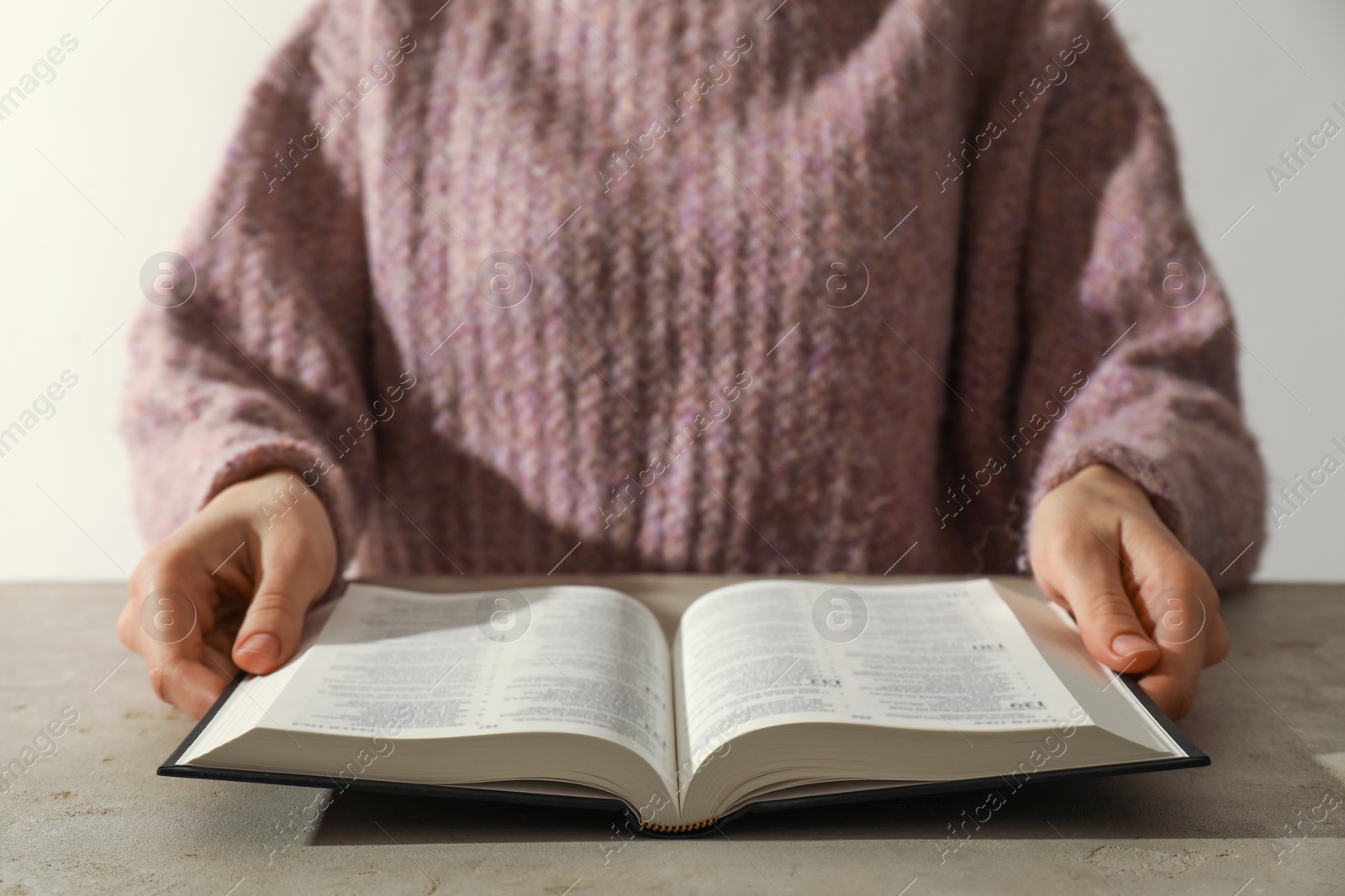 Photo of Woman reading Holy Bible in English language at beige table, closeup