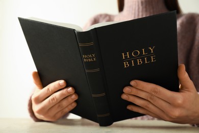 Photo of Woman reading Holy Bible at beige table, closeup