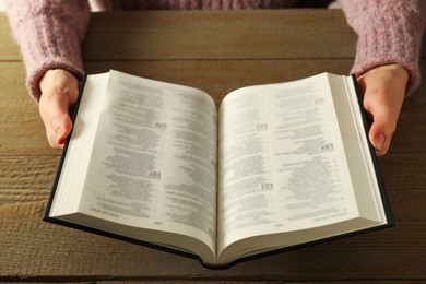 Woman reading Holy Bible in English language at wooden table, closeup