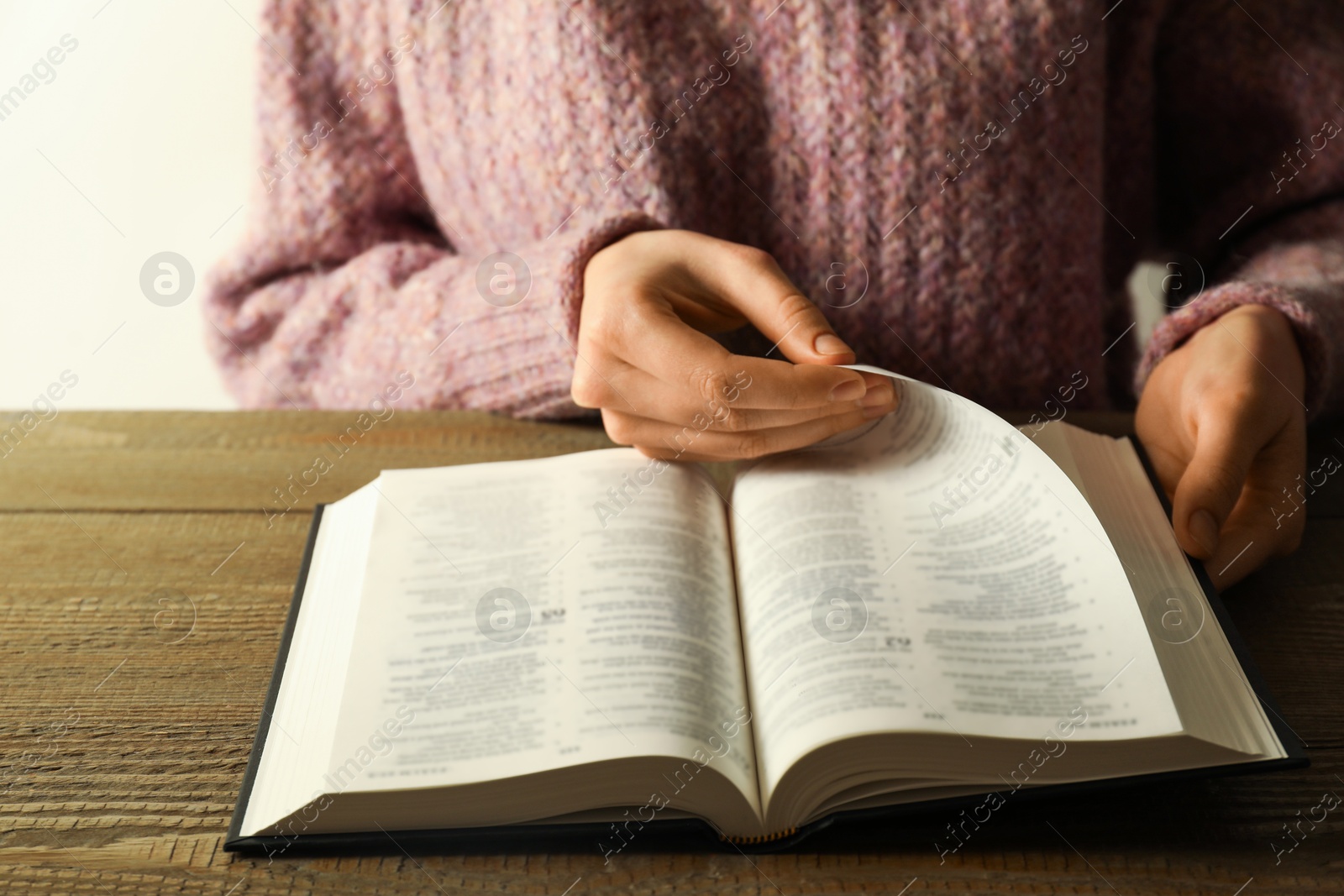 Photo of Woman reading Holy Bible in English language at wooden table, closeup