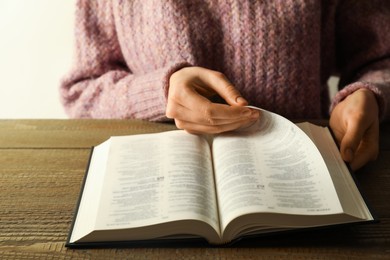 Photo of Woman reading Holy Bible in English language at wooden table, closeup