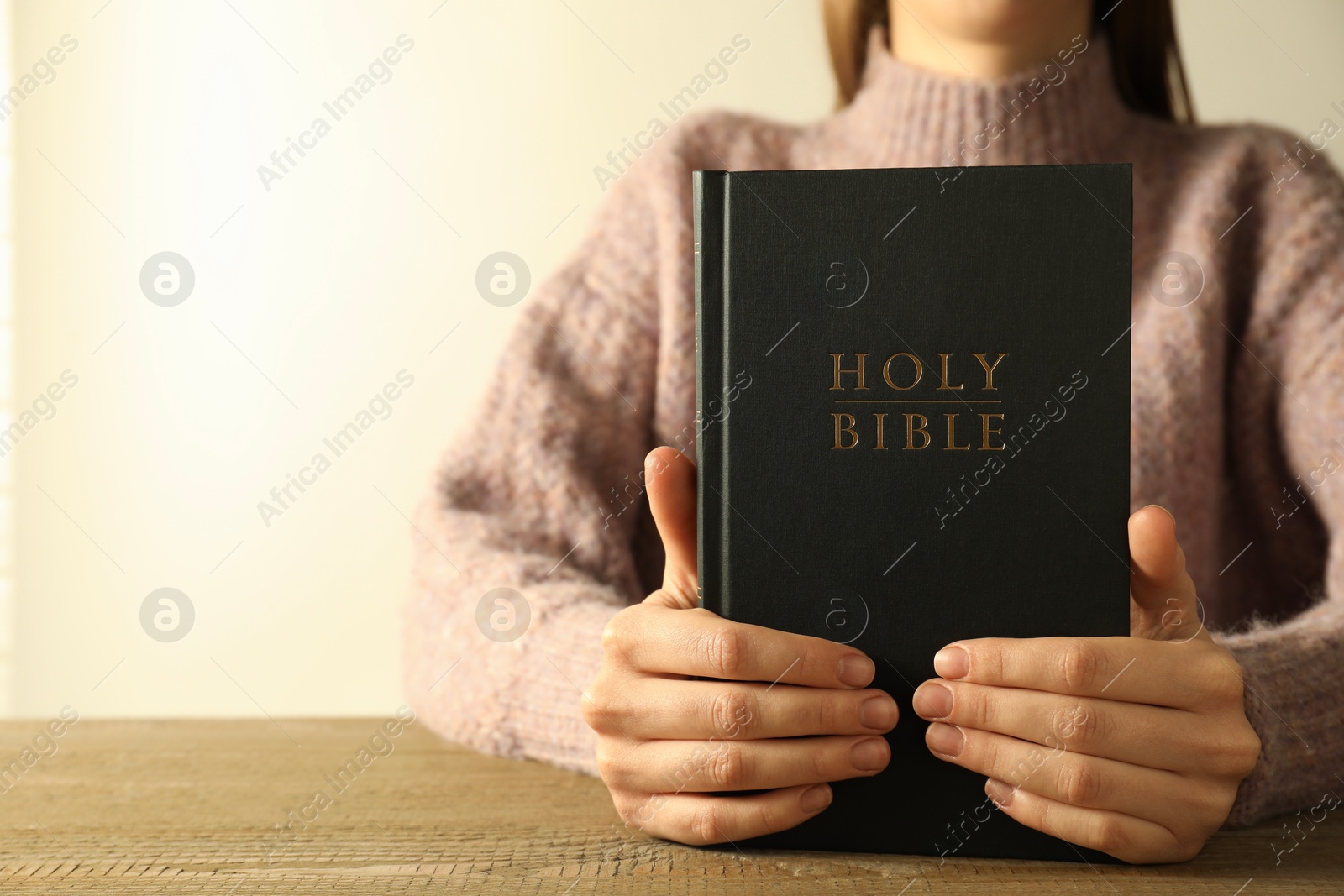 Photo of Woman with hardcover Holy Bible at wooden table, closeup. Space for text