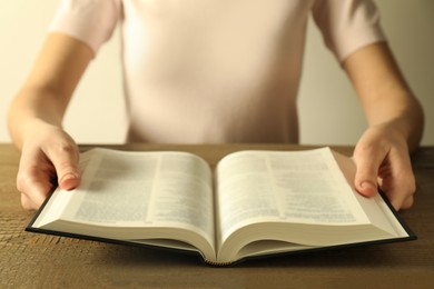 Photo of Woman reading Holy Bible in English language at wooden table, closeup