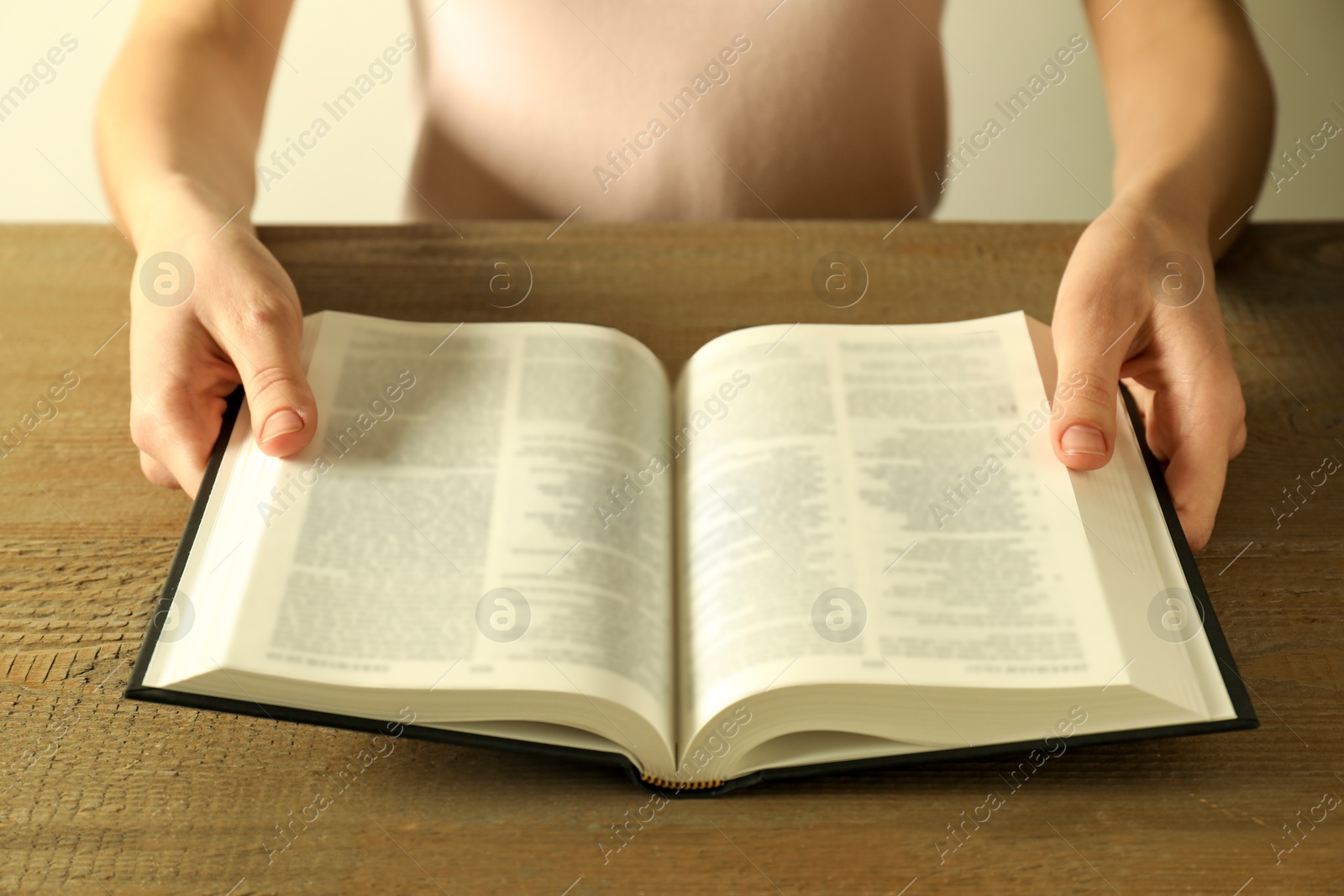 Photo of Woman reading Holy Bible in English language at wooden table, closeup