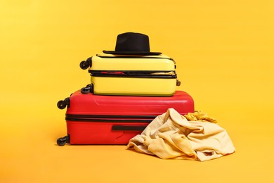 Photo of Packed suitcases with hat and messy clothes on yellow background