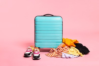 Photo of Suitcase, messy clothes and shoes on pink background