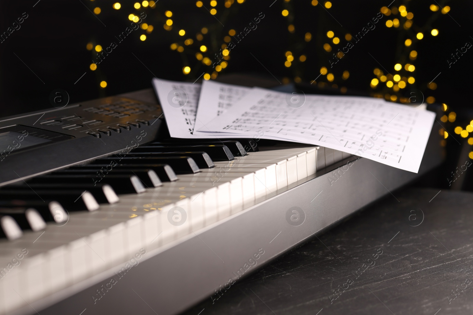 Photo of Sheets with musical notes on piano against blurred lights, closeup. Bokeh effect