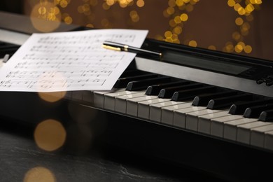 Photo of Sheet with musical notes and pen on piano against blurred lights, closeup. Bokeh effect