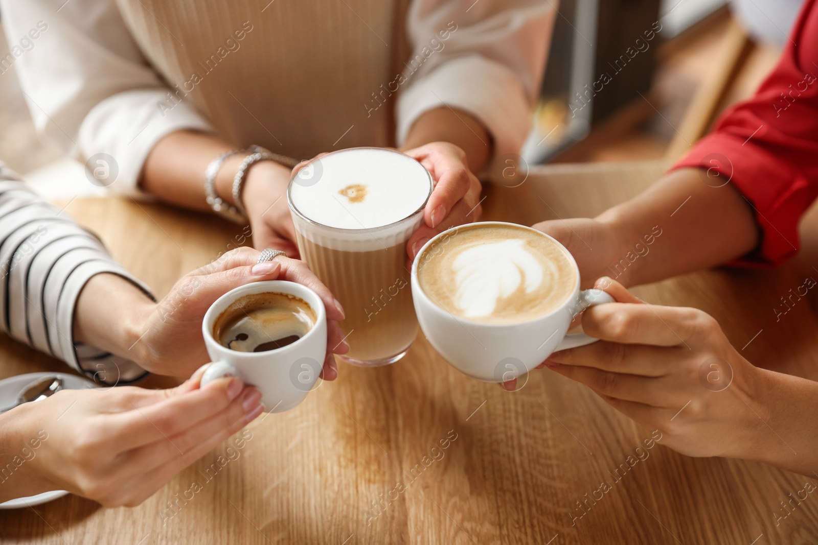 Photo of Women with cups of delicious coffee drinks at wooden table in cafe, closeup