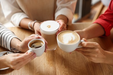 Photo of Women with cups of delicious coffee drinks at wooden table in cafe, closeup