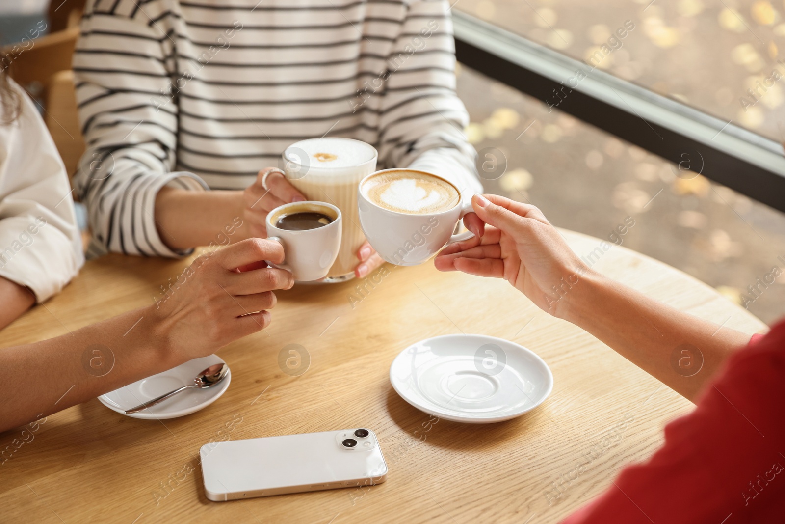 Photo of Women with cups of delicious coffee drinks at wooden table in cafe, closeup