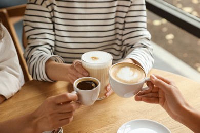 Photo of Women with cups of delicious coffee drinks at wooden table in cafe, closeup