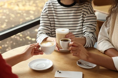 Photo of Women with cups of delicious coffee drinks at wooden table in cafe, closeup