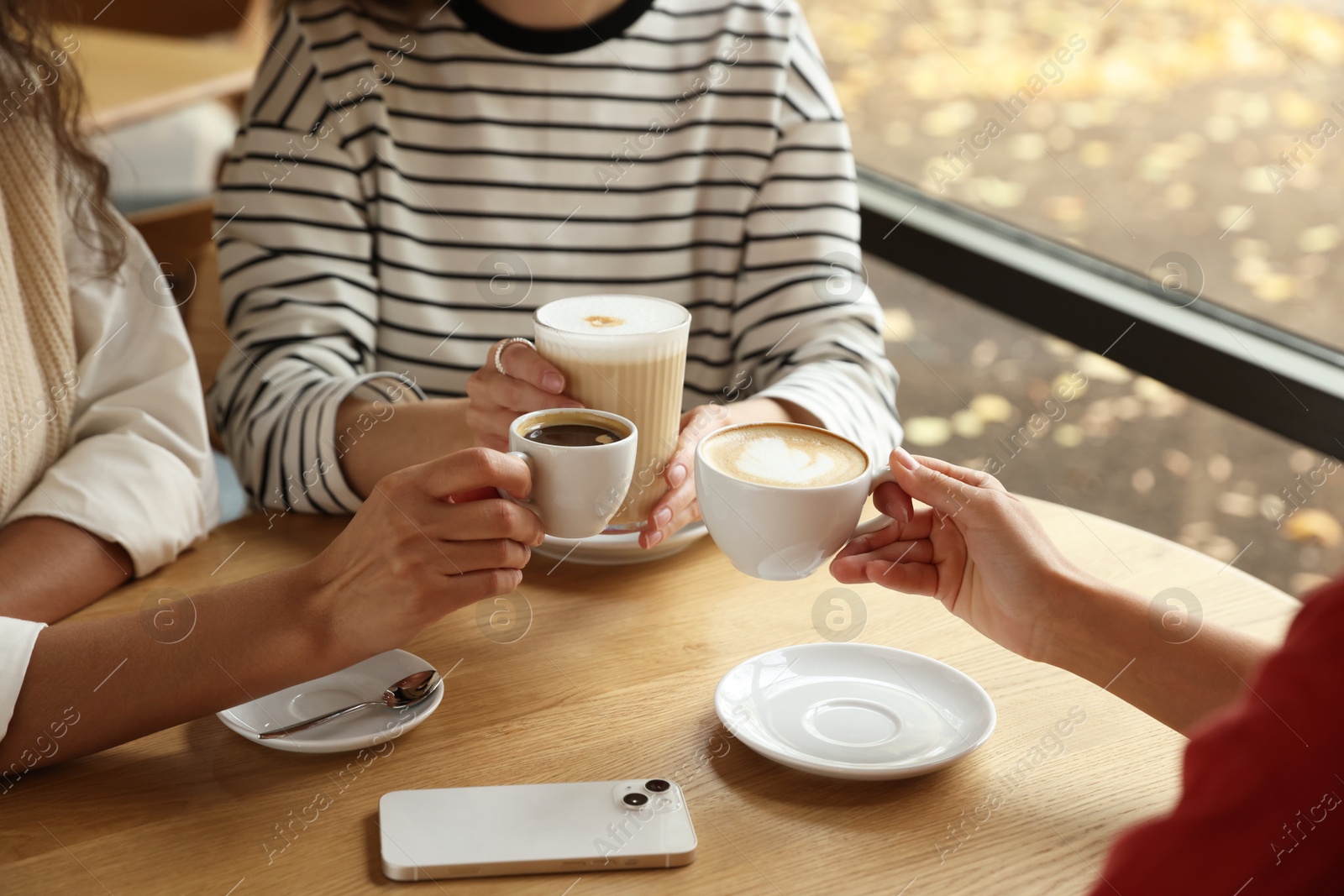 Photo of Women with cups of delicious coffee drinks at wooden table in cafe, closeup