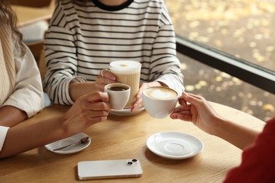 Photo of Women with cups of delicious coffee drinks at wooden table in cafe, closeup