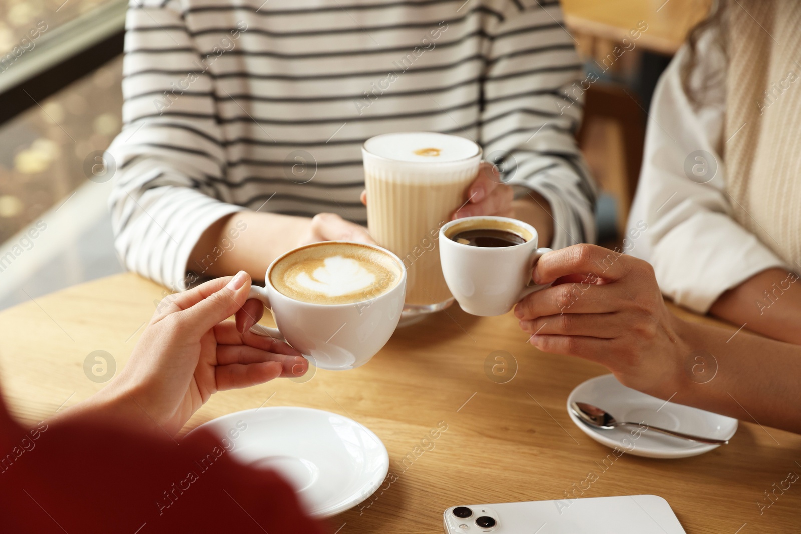 Photo of Women with cups of delicious coffee drinks at wooden table in cafe, closeup