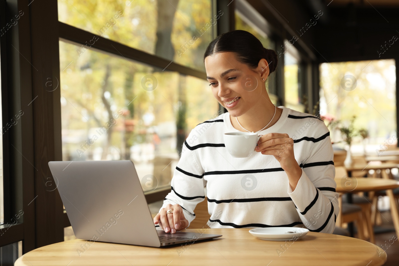 Photo of Woman with cup of coffee working on laptop in cafe