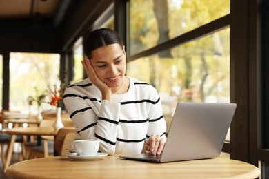 Photo of Woman working on laptop at table in cafe