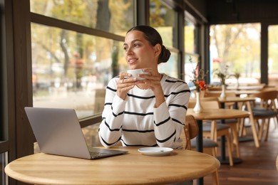 Photo of Woman with cup of coffee working on laptop in cafe