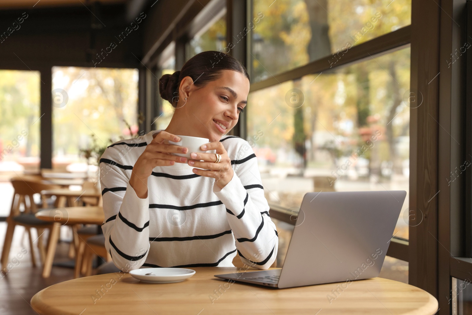 Photo of Woman with cup of coffee working on laptop in cafe