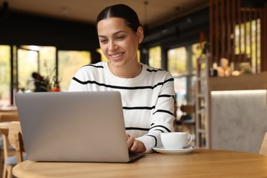 Photo of Woman working on laptop at table in cafe