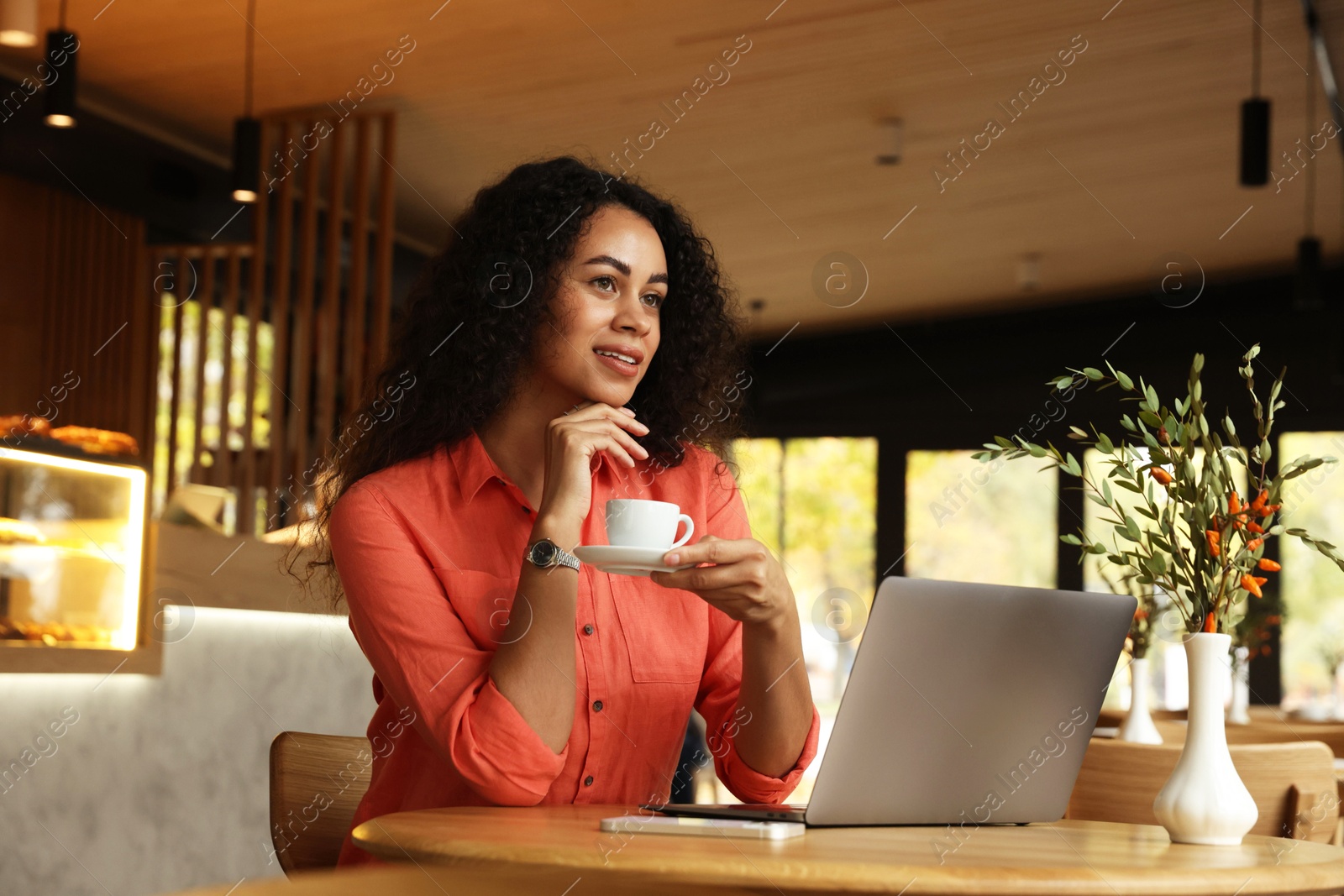 Photo of Woman with cup of coffee working on laptop in cafe