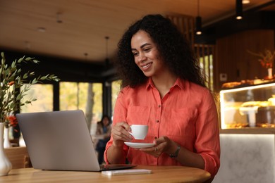 Photo of Woman with cup of coffee working on laptop in cafe