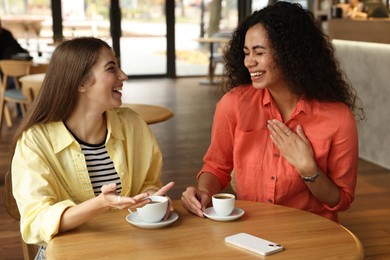 Photo of Happy women with coffee drinks chatting in cafe