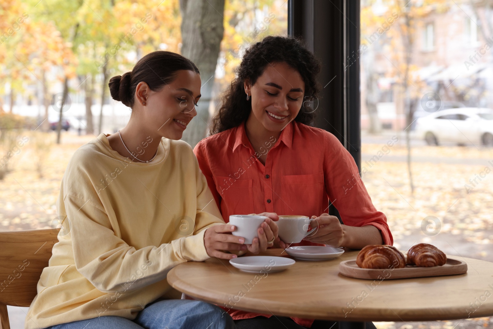 Photo of Happy women with coffee drinks chatting in cafe