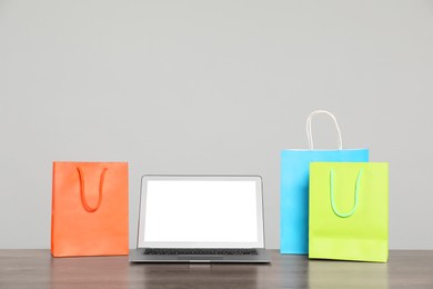 Photo of Internet shopping. Laptop and colorful paper bags on wooden table against grey background