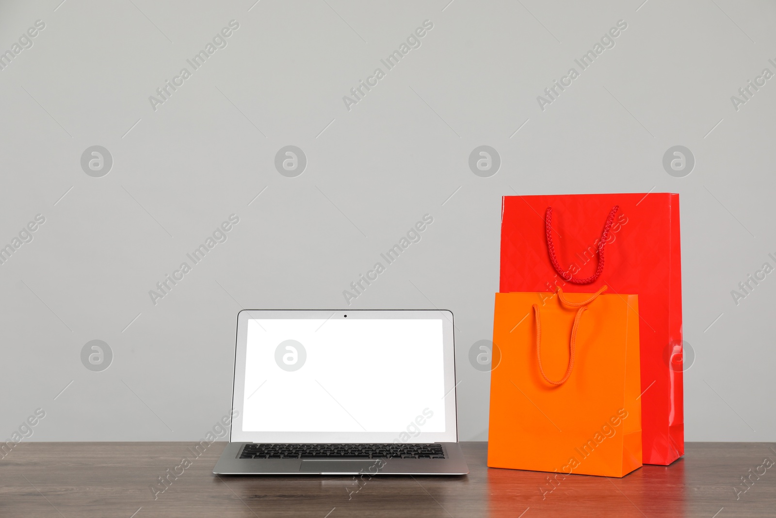 Photo of Internet shopping. Laptop and colorful paper bags on wooden table against grey background