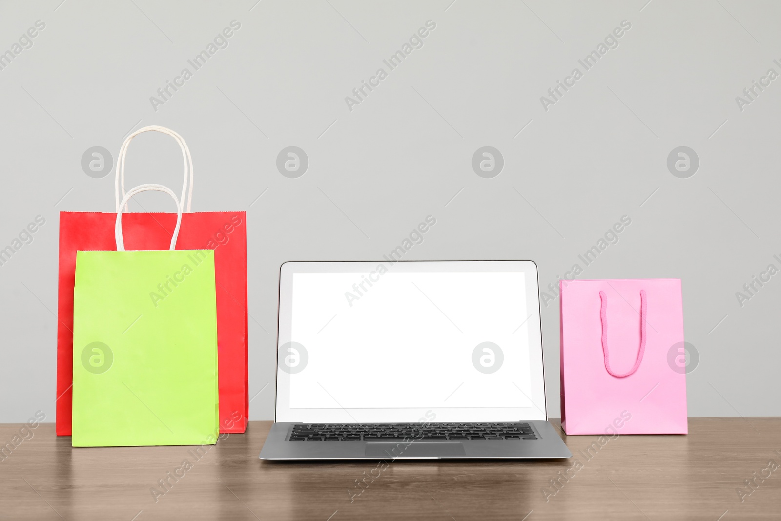 Photo of Internet shopping. Laptop and colorful paper bags on wooden table against grey background