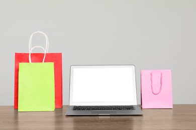 Photo of Internet shopping. Laptop and colorful paper bags on wooden table against grey background