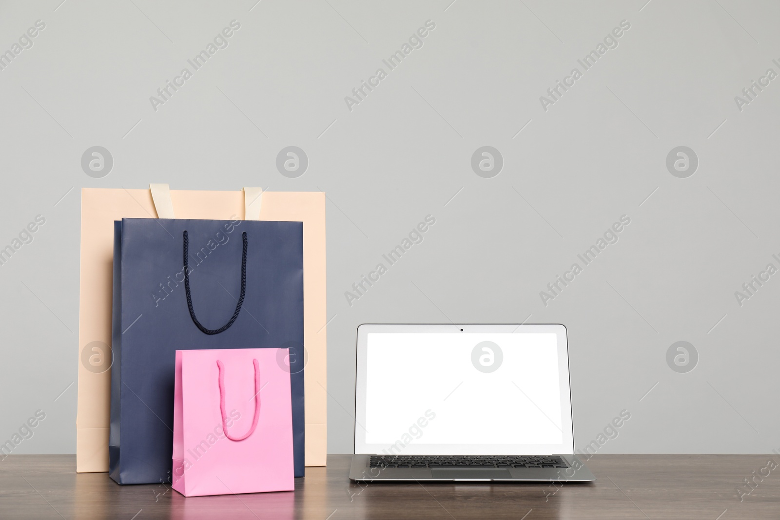 Photo of Internet shopping. Laptop and colorful paper bags on wooden table against grey background