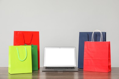 Photo of Internet shopping. Laptop and colorful paper bags on wooden table against grey background