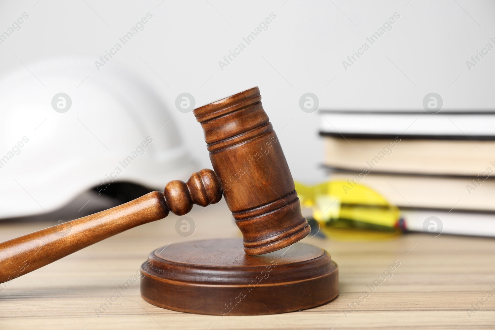 Photo of Accident at work concept. Gavel, books and construction worker's protective gear on wooden table, selective focus