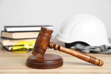 Photo of Accident at work concept. Gavel, books and construction worker's protective gear on wooden table, selective focus