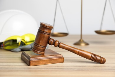 Photo of Accident at work concept. Gavel, scales and construction worker's protective gear on wooden table, selective focus